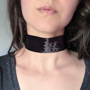 May include: A black velvet choker necklace. The choker is wide and sits close to the neck.
