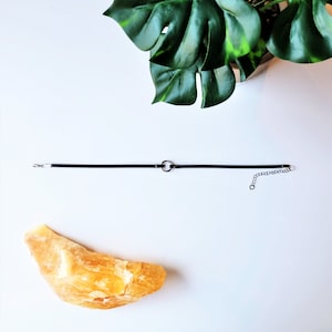 May include: A simple black choker necklace with a silver circle pendant.