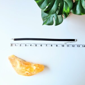 May include: A black velvet choker necklace with a silver chain closure. The necklace is laid out on a white surface with a ruler measuring 12 inches.