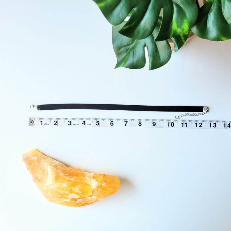 May include: A black velvet choker necklace with a silver chain closure. The necklace is laid out on a white surface with a ruler measuring 12 inches.