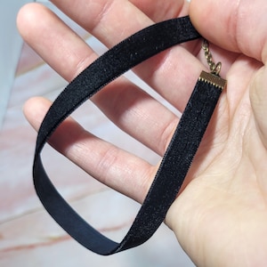 Puede incluir: Un collar gargantilla de terciopelo negro con un cierre y cadena de color dorado. La gargantilla est&aacute; hecha de un material suave y aterciopelado y est&aacute; dise&ntilde;ada para quedar cerca del cuello. El collar es un accesorio sencillo pero elegante.