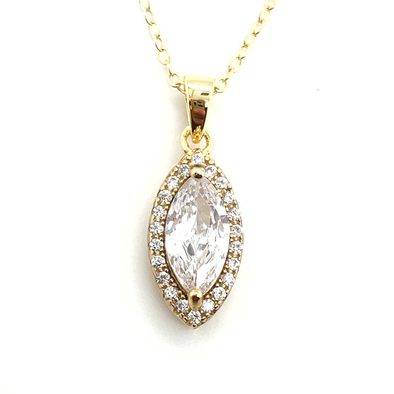 May include: A gold-colored necklace with a pendant featuring a large, clear, marquise-cut stone surrounded by smaller, clear stones. The pendant is suspended from a delicate gold chain, creating an elegant and eye-catching piece of jewelry.