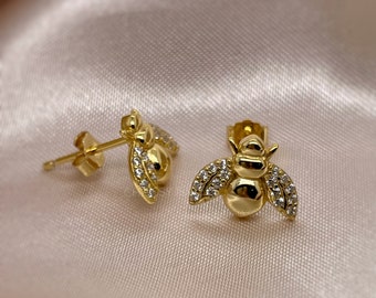 Op de afbeelding: Een paar gouden bijen oorbel studs met heldere zirkonia stenen. De bijen zijn gedetailleerd met vleugels en een textuur lichaam.