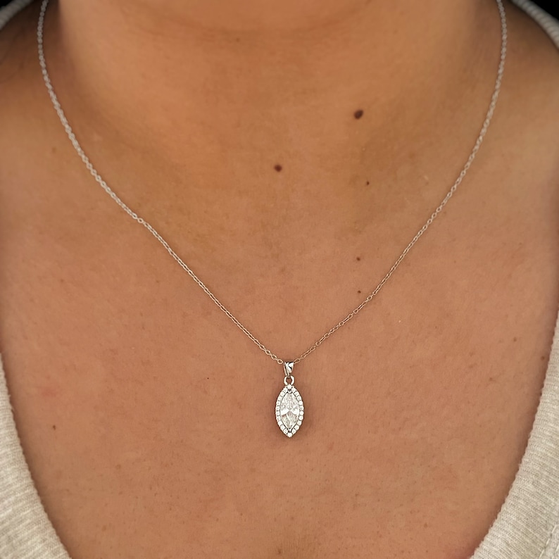 May include: A silver necklace with a pendant featuring a marquise-shaped design. The pendant is encrusted with small, clear gemstones, and the necklace is displayed against a skin tone background.