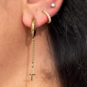 May include: Gold hoop earrings with a dangling chain and an ankh charm.