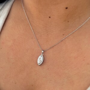 May include: A silver necklace with a pendant featuring a marquise-shaped clear stone surrounded by smaller clear stones. The pendant hangs from a delicate silver chain, creating a classic and elegant look. The necklace is displayed against a skin tone background.