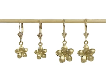 May include: Three pairs of gold-tone earrings with a flower design. The earrings are hanging from a wooden dowel.