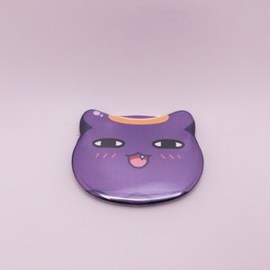 May include: Purple cat-shaped button with a mischievous expression, featuring a small orange halo and blushing cheeks.