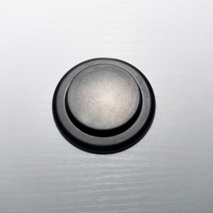 May include: A black round button with a raised center. The button has a smooth, matte finish.