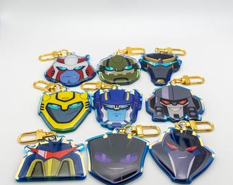 May include: A collection of nine acrylic keychains featuring stylised robot character faces in various colours including yellow, blue, grey, green, and black. Each keychain is attached to a gold-coloured metal lobster clasp for easy attachment.