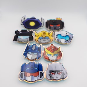 May include: A set of eight Transformers character pins featuring various characters from the franchise. The pins are made of metal and have a glossy finish. The characters include Optimus Prime, Megatron, Bumblebee, Starscream, Soundwave, Ironhide, Ratchet, and Jazz.