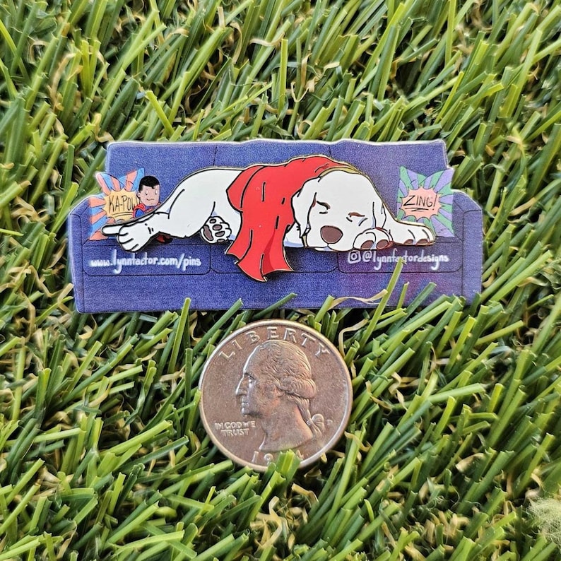 May include: A pin depicting a white dog in a red cape, resting on a blue sofa. The pin includes comic book sound effects and the text "www.lynnfordesigns.com/pins" and "@lynnfordesigns".