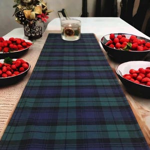 May include: A blue and green plaid table runner with red berries in bowls on a wooden table.