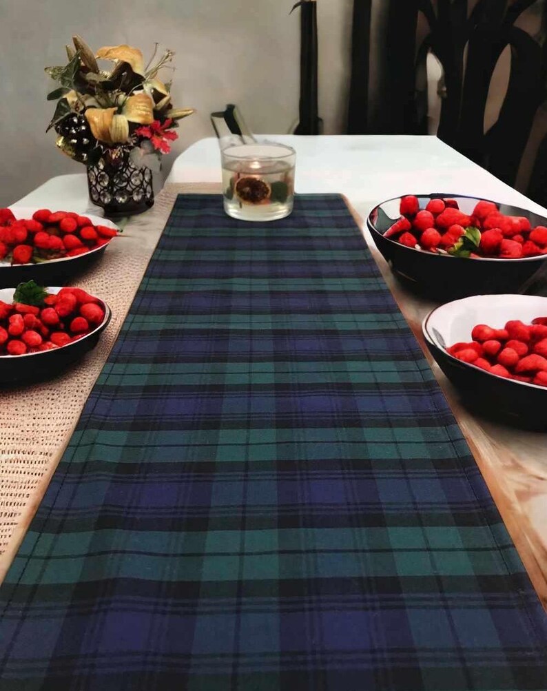 May include: A blue and green plaid table runner with red berries in bowls on a wooden table.