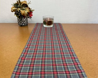 May include: A red, gray, and yellow plaid table runner. The runner is on a brown wooden table.