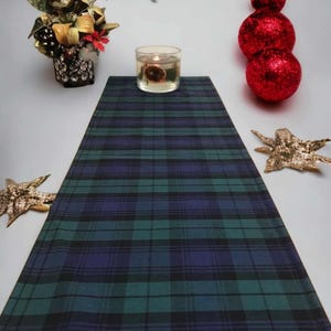 May include: A green, blue, and black plaid table runner with a candle in a clear glass jar on top of it.