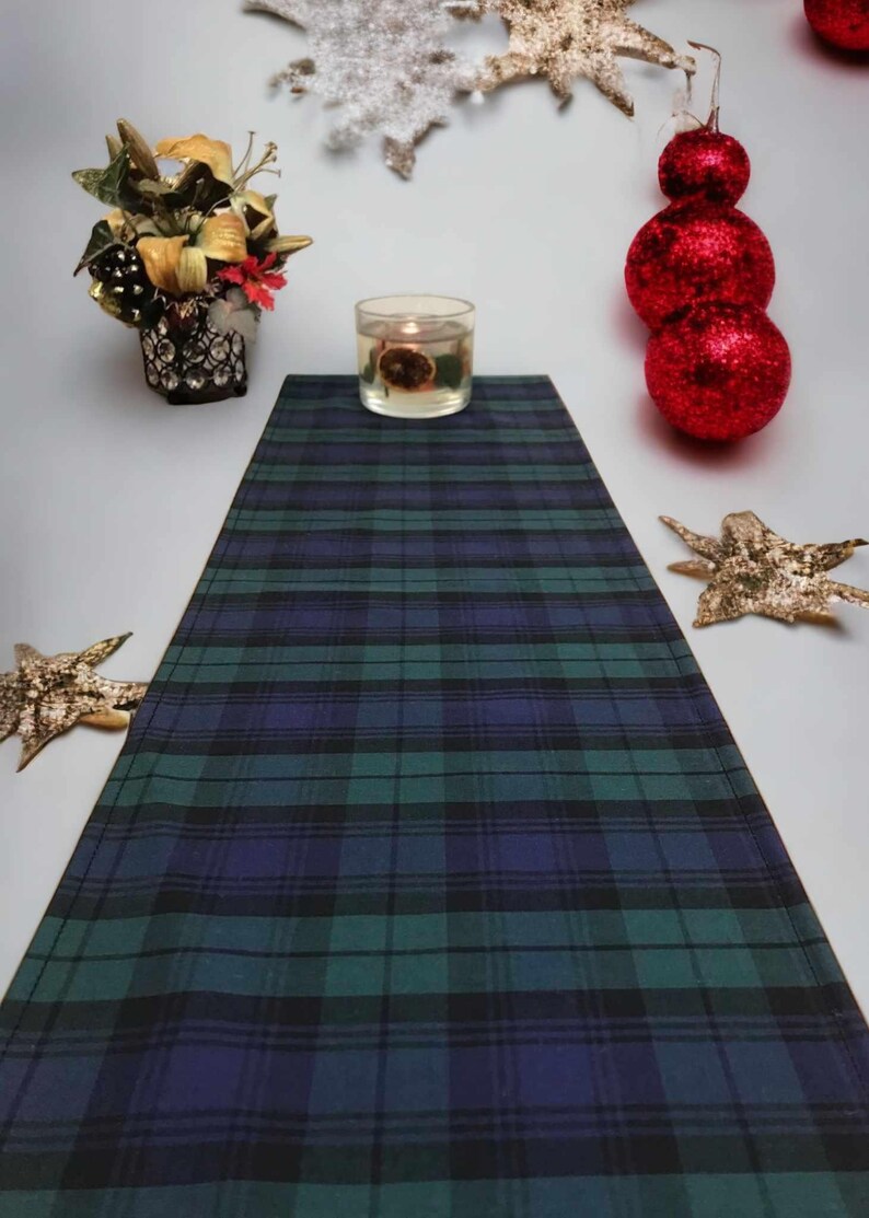 May include: A green, blue, and black plaid table runner with a candle in a clear glass jar on top of it.