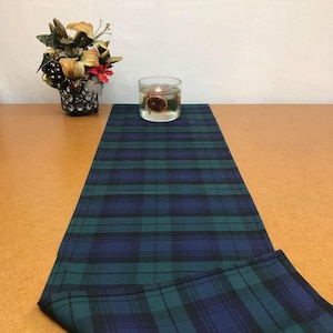 May include: A green and blue plaid table runner with a decorative candle in a glass jar on top of it.