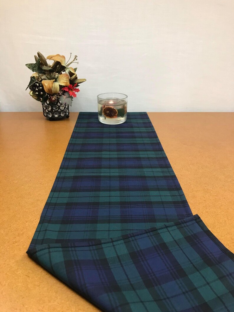 May include: A green and blue plaid table runner with a decorative candle in a glass jar on top of it.