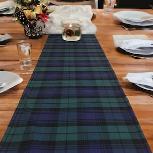 May include: A green, blue, and black plaid table runner with a clear glass candle holder in the center.