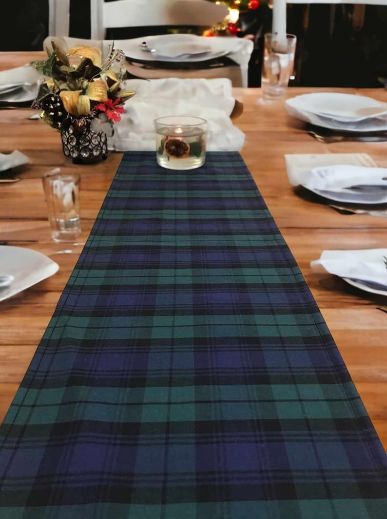May include: A green, blue, and black plaid table runner with a clear glass candle holder in the center.