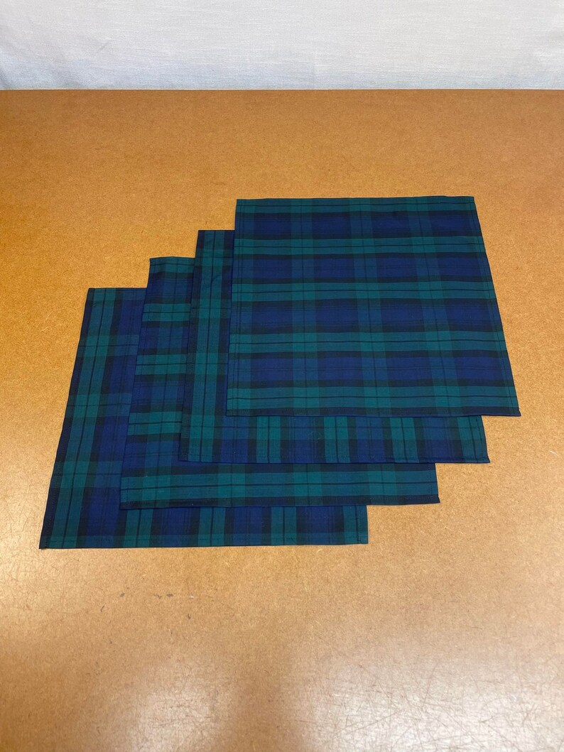 May include: Four plaid fabric handkerchiefs in shades of green and blue, stacked on top of each other.