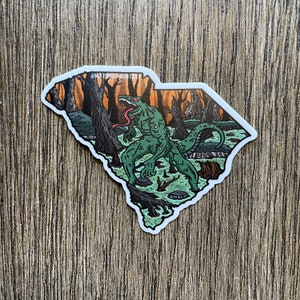 May include: A green monster with a long tongue and sharp teeth stands in a swampy forest. The monster is in the shape of the state of South Carolina. The background is a sunset with orange and yellow colors.