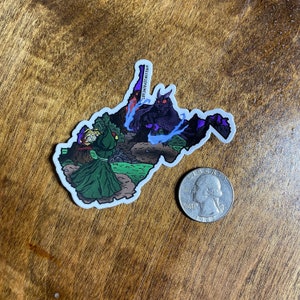May include: A sticker of the state of West Virginia with a green monster fighting a purple monster. The sticker has the text "@MAKINGSPRIMEART" on it.