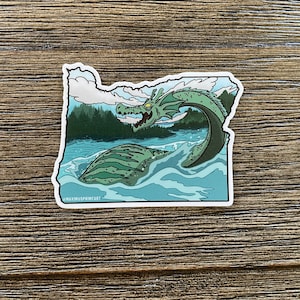 May include: A green and blue sticker featuring a cartoon illustration of a sea monster in the shape of the state of Oregon. The sticker includes the text "@MAXIMUSPRIMEART".