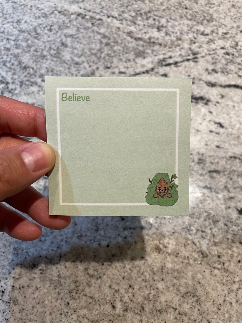 May include: A green notecard with a white border and the word "Believe" printed in green. A cartoon character is peeking out from behind a bush in the bottom right corner.