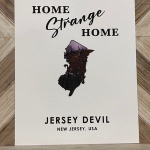 May include: A white print with black text that reads "Home Strange Home" and "Jersey Devil, New Jersey, USA". The print features a silhouette of the state of New Jersey with a red devil inside.