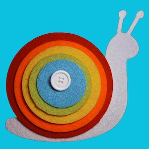 May include: A whimsical felt snail with a rainbow-colored shell and a white button. The snail's body is white, and the shell features concentric circles in red, orange, yellow, green, and blue. The background is a solid teal color.