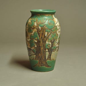 May include: A ceramic vase featuring a relief design of trees with brown trunks and green foliage against a cream and tan background. The vase has a cylindrical body with a tapered neck and a solid green base, showcasing a textured surface.