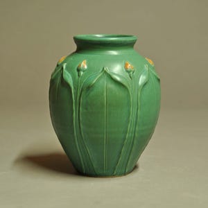 May include: A matte green ceramic vase with a rounded body and a narrow neck. The exterior features a raised relief pattern of vertical leaves and small, orange-tipped flower buds that extend from the base toward the rim of the vessel.