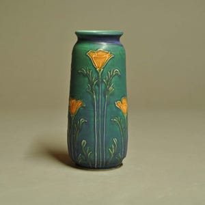 May include: A tall, cylindrical vase with a green and blue glaze. The vase features a design of orange poppy flowers and stems. The vase is approximately 10 inches tall and has a narrow neck.
