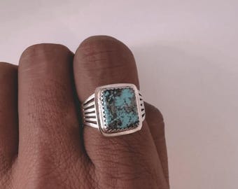 May include: A silver ring with a turquoise stone set in a square shape. The ring has a band with multiple grooves.