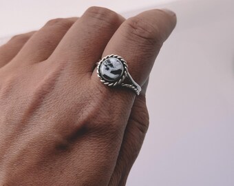May include: A silver ring with a white and black stone set in a rope-like design.
