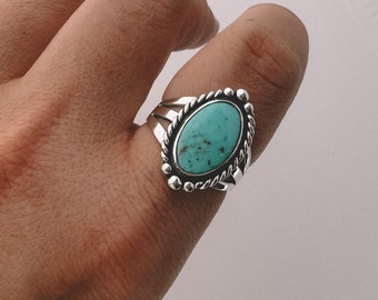 Puede incluir: Un anillo de plata con una piedra turquesa engastada en un diseño ovalado detallado.