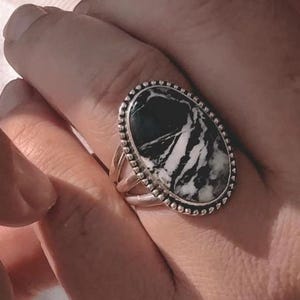 Può includere: Un anello d'argento con una pietra ovale nera e bianca incastonata in una ghiera con perline. La pietra ha un motivo a spirale.