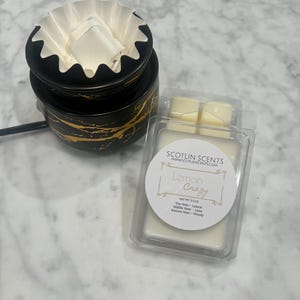May include: Two white wax melts in a clear plastic container with a label that reads "Lemon Crazy" and "NET WT. 2.5 OZ" with the scent notes listed below. Top Note - Lemon, Middle Note - Lime, Bottom Note - Woody. SCOTLIN SCENTS WWW.SCOTLINSCENTS.COM