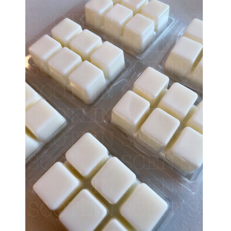 May include: A set of six white wax melts in a clear plastic packaging. The wax melts are in the shape of cubes and are arranged in a grid pattern.