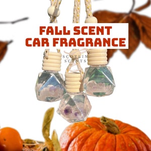 May include: Three clear glass car air fresheners with purple crystals inside. The air fresheners are hanging from a string and have a wooden cap. The text "SCOTLIN SCENTS" is visible on the middle air freshener. The image is captioned "FALL SCENT CAR FRAGRANCE".