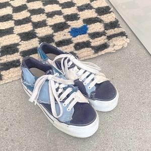 Könnte beinhalten: Ein Paar blaue und schwarze Patchwork-Sneaker mit weißen Schnürsenkeln. Die Sneaker bestehen aus verschiedenen Teilen aus Denim und Canvas.