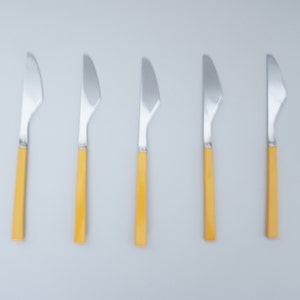 Könnte beinhalten: Fünf silberne Buttermesser mit gelben Kunststoffgriffen.