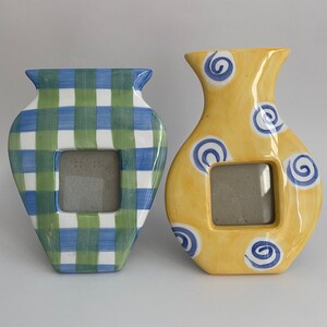 Peut inclure: Deux cadres photo en céramique en forme de vases. L'un est jaune avec des tourbillons bleus et l'autre est blanc avec un tissu écossais vert et bleu. Les deux ont une ouverture rectangulaire pour une photo.