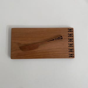 Puede incluir: Una tabla de servir de madera con un borde decorativo y un cuchillo de mantequilla de madera a juego.