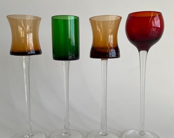 Pode incluir: Quatro copos altos com haste e copas de vidro de diferentes cores. Os copos são transparentes com uma base redonda. As copas são âmbar, verde, âmbar e vermelho.
