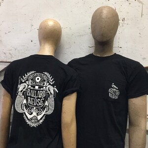 May include: Two black t-shirts with a white graphic design on the back and front. The back design features an anchor with the text "Architectural Salvage Ballard Reuse" and the front design features a bird with the text "Ballard Reuse".