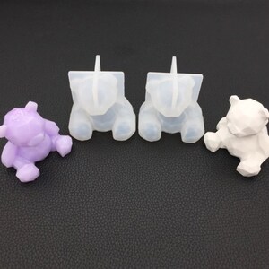 May include: A collection of bear-shaped items. There is a purple bear, two clear silicone molds, and a white bear. All bears have a geometric, faceted design. The items are arranged on a dark, textured surface.