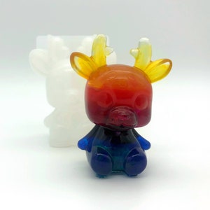 May include: A colorful resin deer figurine with a gradient of red, orange, and blue hues. The deer has yellow antlers and a cute, rounded design. A white deer-shaped mold is in the background.